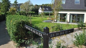 A residential area with a paved pathway, a signpost indicating directions, and a modern house with a garden. - Bungalow in Texel Near National Park Dunes (De Koog)