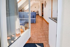 A hallway with a checkered curtain, a blue sofa, a wooden floor, and a white door.