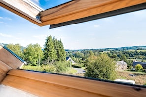 A view through a window with a wooden frame, overlooking a rural landscape with houses, trees, and a road.