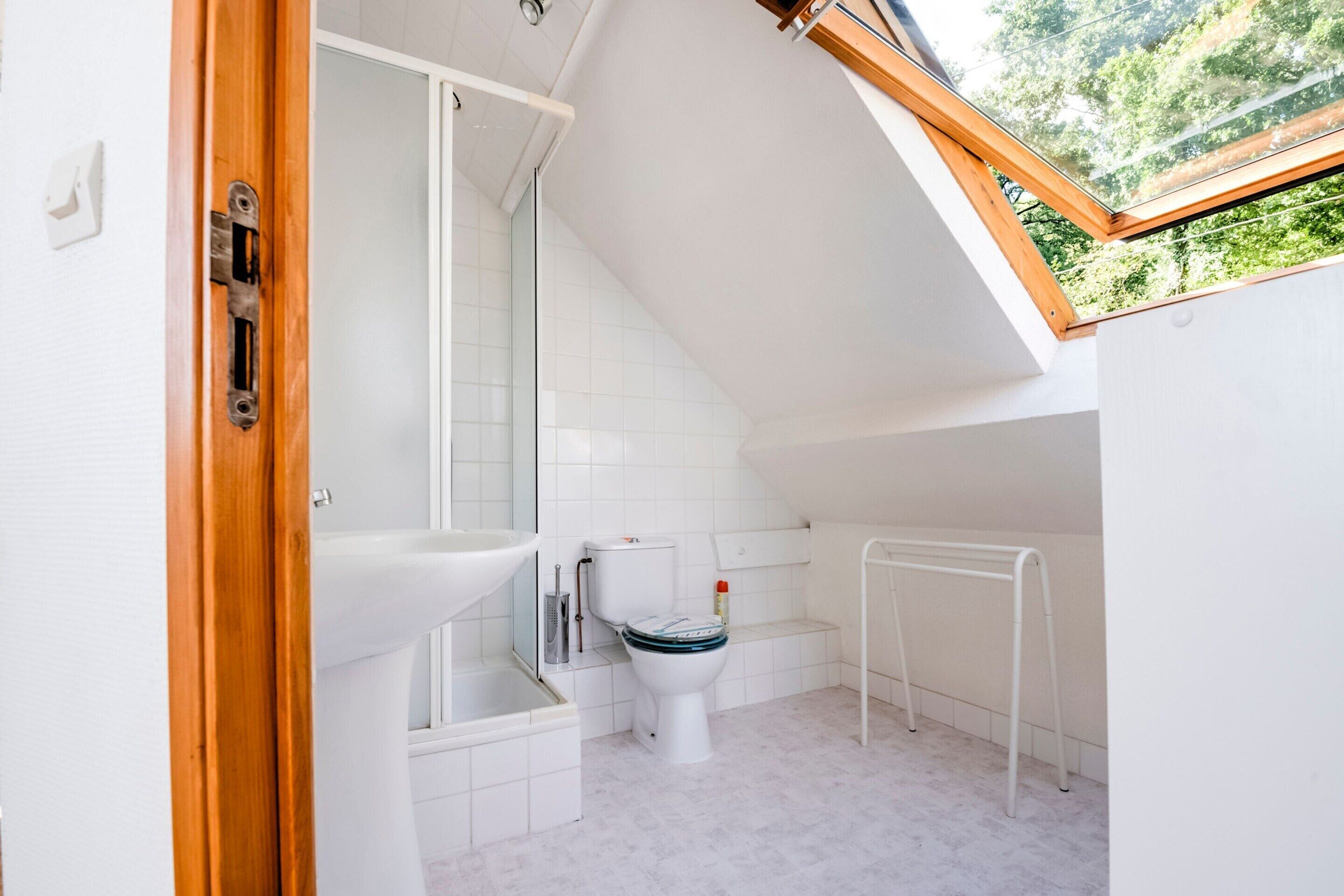 Un baño pequeño y moderno con tragaluz, sanitarios blancos y zona de ducha.