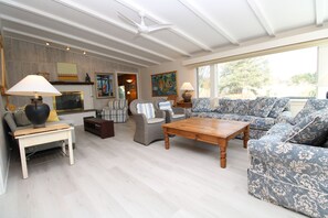 A spacious living room with a wooden coffee table, two sofas, a fireplace, and a ceiling fan.
