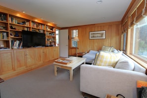 A living room with a sofa, a television, wooden bookshelves, and a window.
