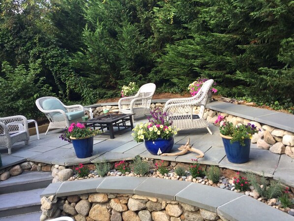 An outdoor patio area with stone steps, wicker furniture, and potted plants.