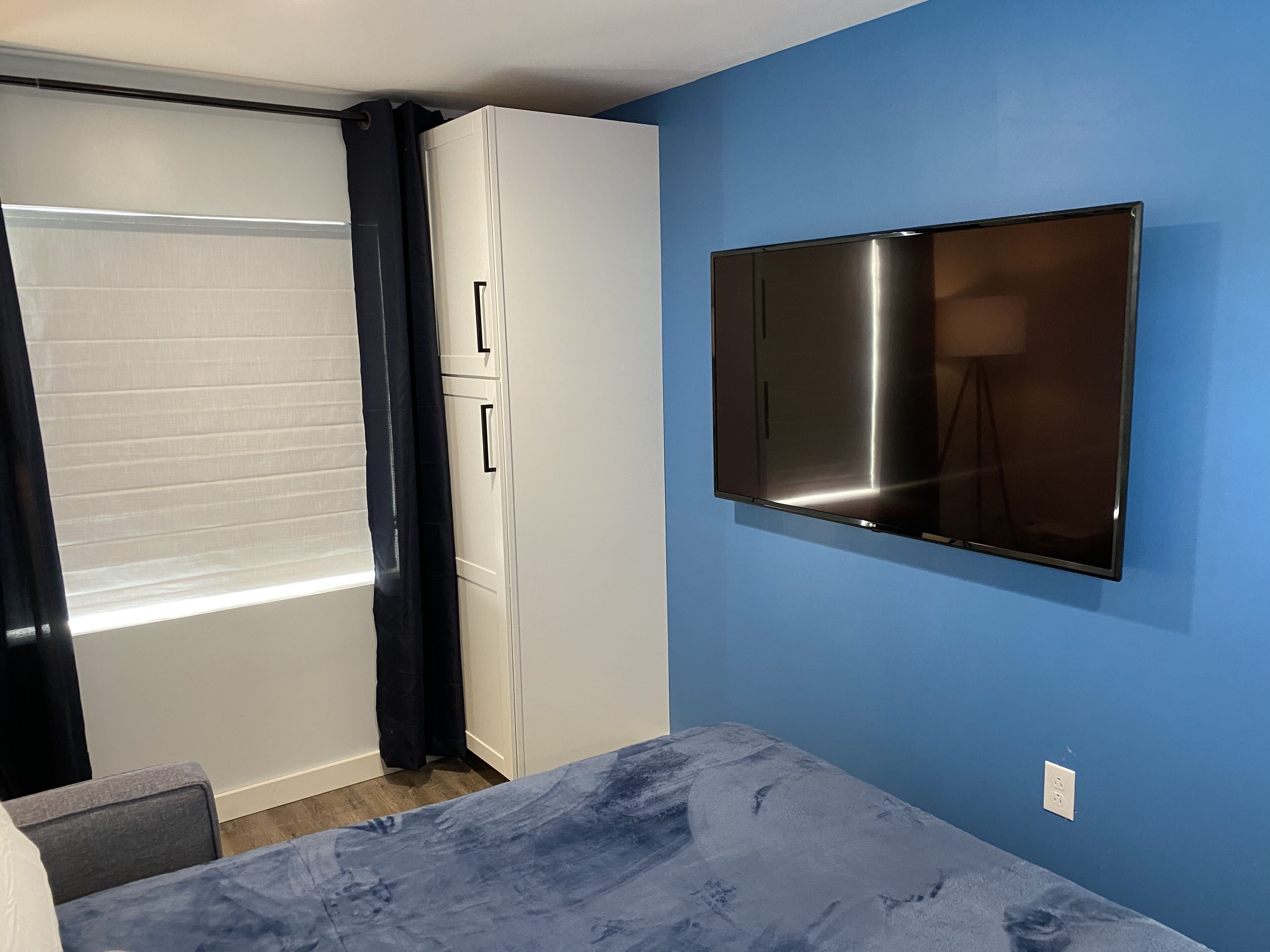 A bedroom with a bed, a wardrobe, a television, and a window with curtains.