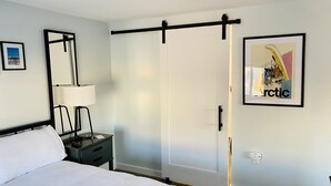 A hotel room with a bed, bedside table, lamp, and a sliding door closet. - Noxapaga Suites (Nome)