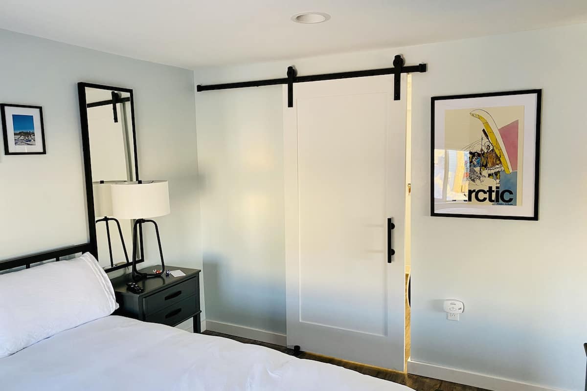 A hotel room with a bed, bedside table, lamp, and a sliding door closet.