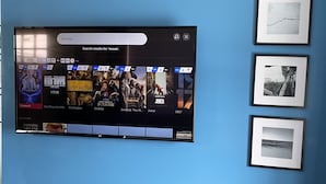 A flat-screen TV mounted on a blue wall displaying a movie streaming service interface with various movie options. - Noxapaga Suites (Nome)