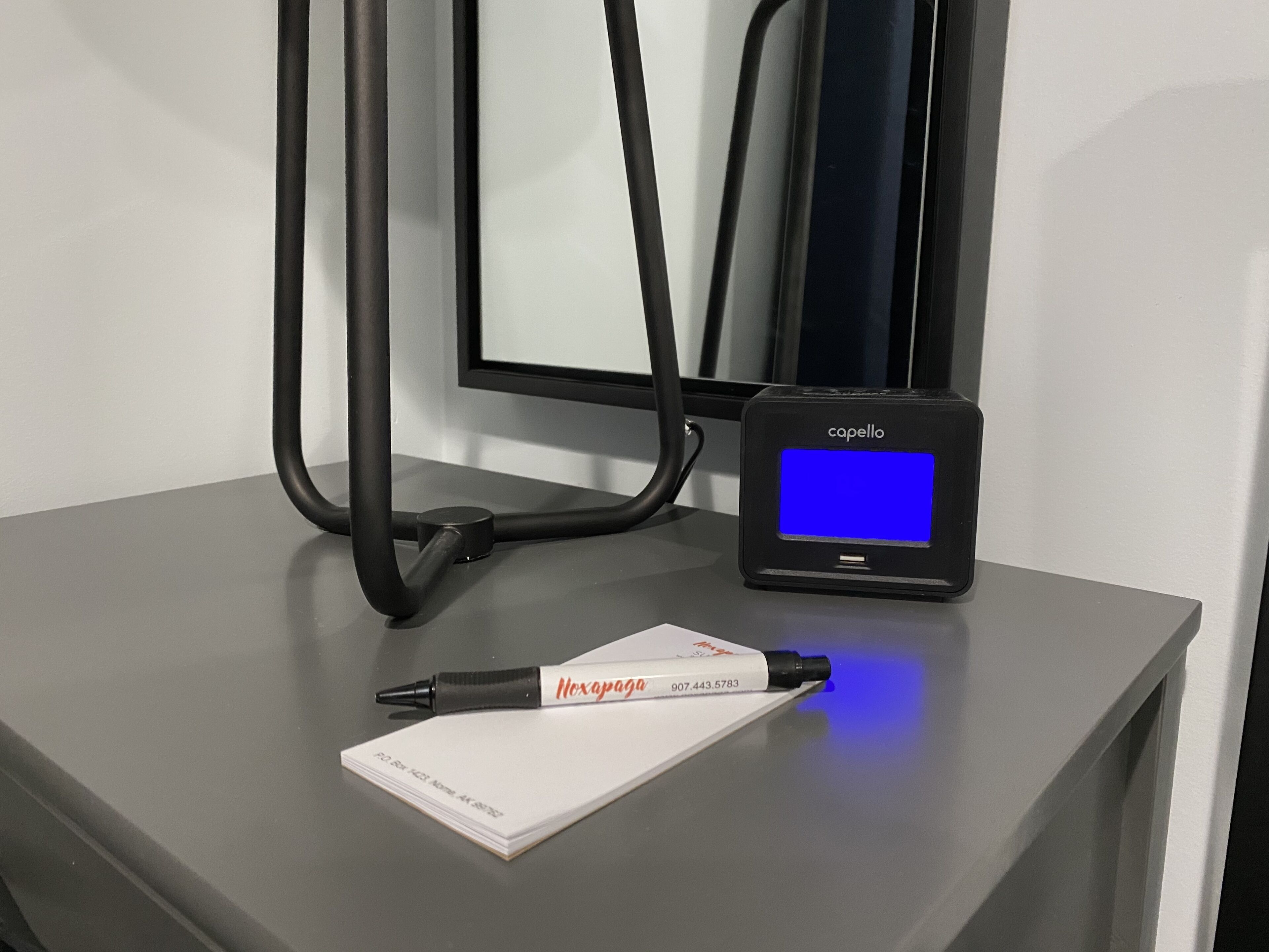 A desk with a pen, a notepad, and a device displaying 'capello' on a blue screen.