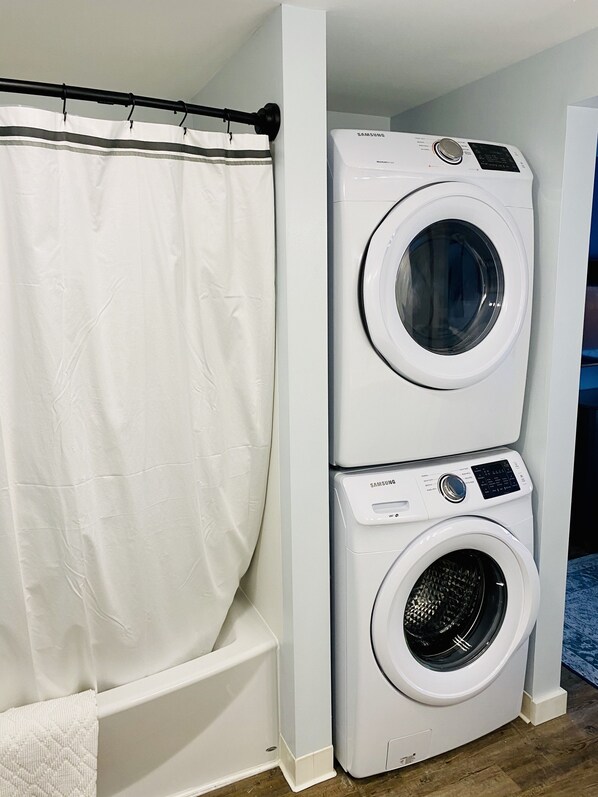 Lavadora y secadora apiladas en un cuarto de lavado con cortina de ducha blanca.