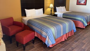 A hotel room with two beds, a red armchair, and a small table with a lamp. - Kenedy Country Inn (Kenedy)