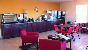 A dining area with red chairs and tables, a kitchen counter with appliances, and a clock on the wall. - Kenedy Country Inn (Kenedy)
