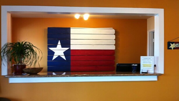 A reception desk with a Texas flag mural, a potted plant, and a sign on the wall. - Kenedy Country Inn (Kenedy)