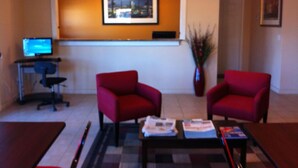 A living room with two red armchairs, a coffee table with magazines, a computer desk with a monitor, and a framed picture on the wall. - Kenedy Country Inn (Kenedy)