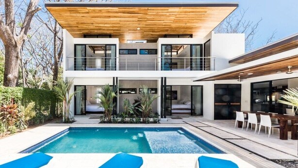 Ett modernt hus i två våningar med en swimmingpool, utomhusmöbler och en träaltan.