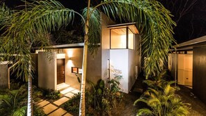 A modern house with a well-lit entrance, surrounded by lush greenery. - FLOW - Main House, For Love Of Waves | Town Center (Nosara)