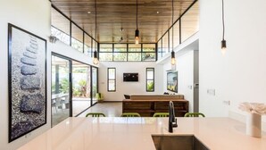 A modern kitchen with a large island, pendant lighting, and a view of the outdoors. - Flow - Casita, For Love Of Waves (Nosara)