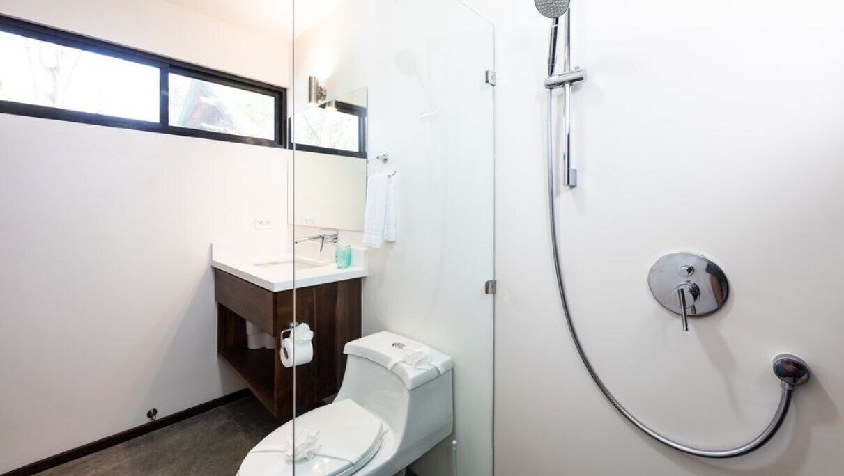 Un baño moderno con cabina de ducha de vidrio, inodoro blanco y tocador de madera.