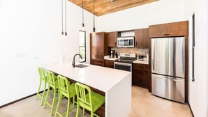 A modern kitchen with a central island, stainless steel appliances, and green chairs. - Flow - Casita, For Love Of Waves (Nosara)