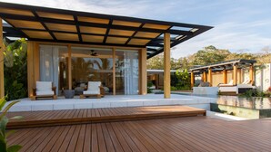 A modern outdoor deck with wooden flooring, a covered seating area with white cushioned chairs, and a pool. - Nai'a, Private entrance to Beach, Gated Comunity (Nosara)