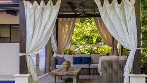 A covered outdoor seating area with a sofa, wicker furniture, and a table with a decorative bowl. - El NIDO, Pristine Beach Nearby (Nosara)