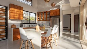 A modern kitchen with wooden cabinets, a large island, and a stainless steel refrigerator. - El NIDO, Pristine Beach Nearby (Nosara)