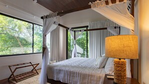 A bedroom with a canopy bed, a bedside lamp, and a view of greenery outside. - El NIDO, Pristine Beach Nearby (Nosara)