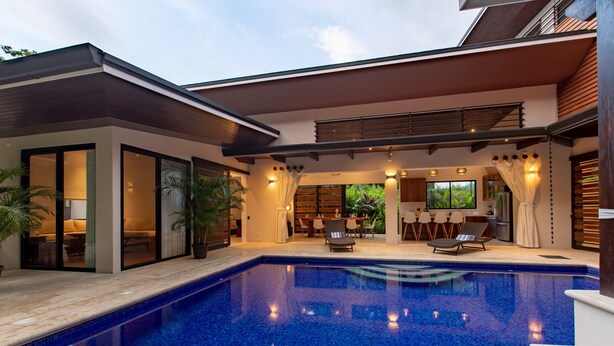 A modern pool area with a clear blue pool, lounge chairs, and a covered seating area with a view of the greenery. - El NIDO, Pristine Beach Nearby (Nosara)