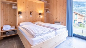 A wooden cabin bedroom with two beds, a wardrobe, a heater, and a view of a village through a window. - Superior Chalet at Kreischberg (Sankt Georgen am Kreischberg)