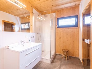 Casa de banho moderna com decoração em madeira, cabine de duche em vidro e toucador branco.