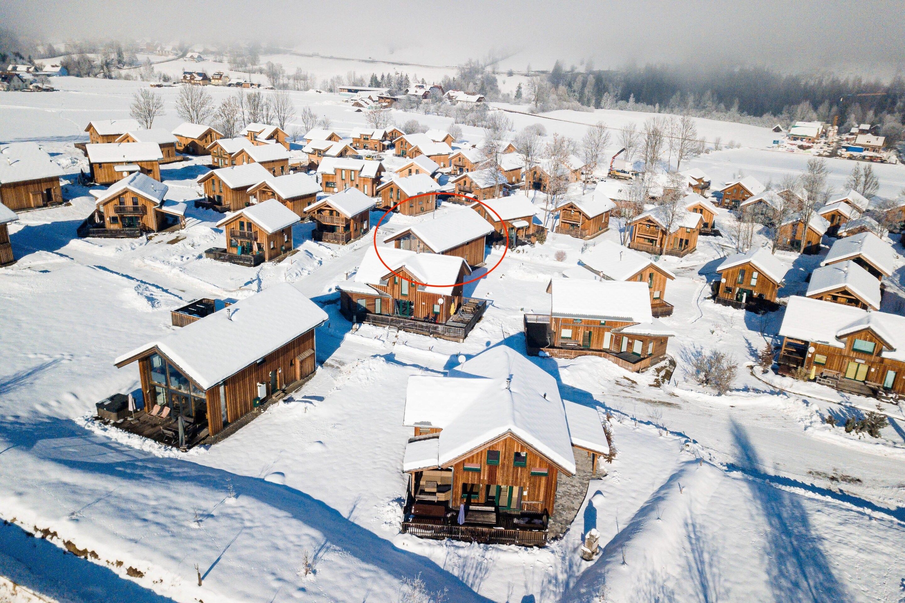 Een besneeuwd dorpje met houten huisjes, een skilift en een helder uitzicht op het besneeuwde landschap.