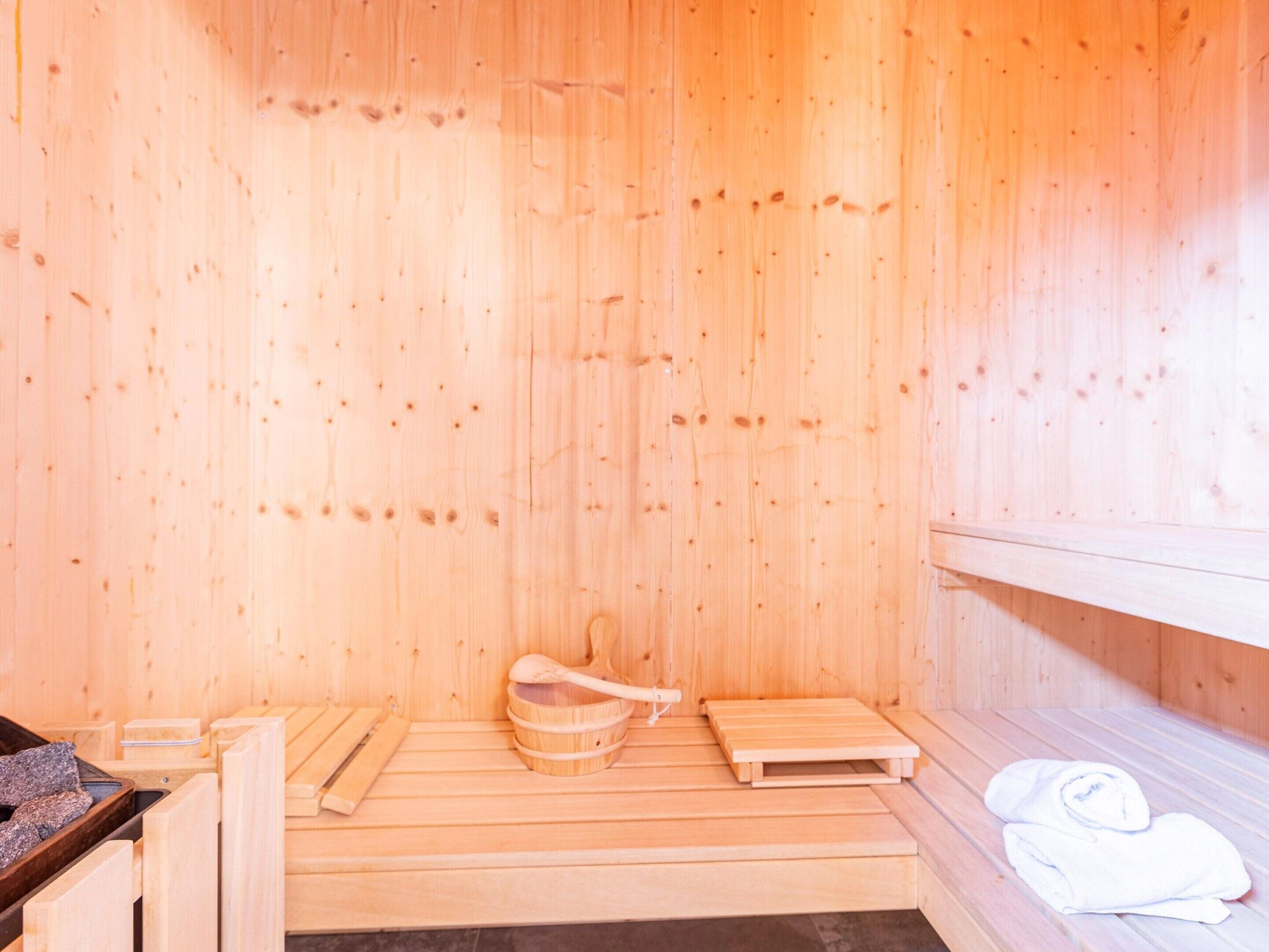 A wooden sauna with benches, a wooden basin, and towels.