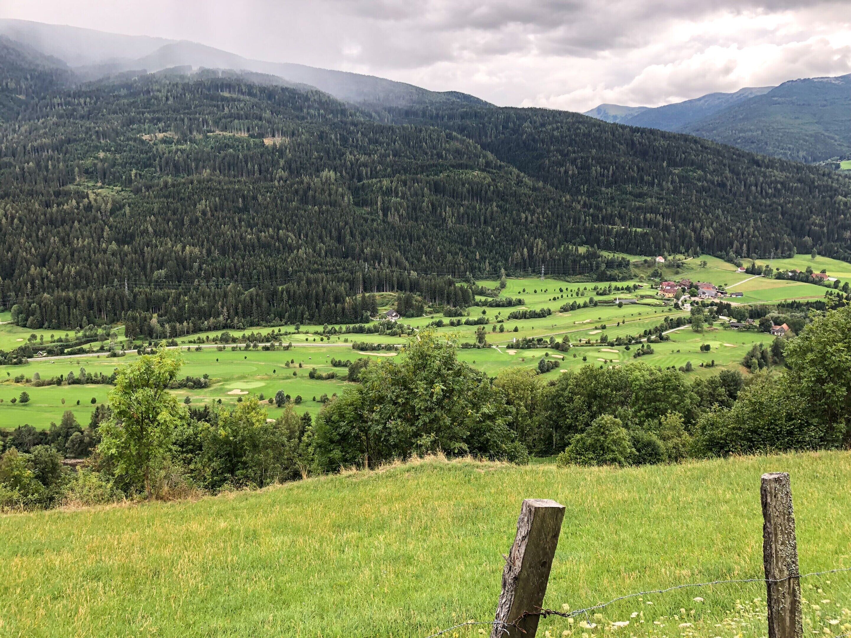 A rural landscape with a valley, green fields, and a forested mountain range.