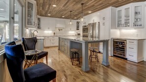 A modern kitchen with white cabinets, a wooden ceiling, and a large island with stools. - Lake Norman Luxury - Large Saltwater Pool, Dock & Boathouse - Sleeps 18 (Denver)