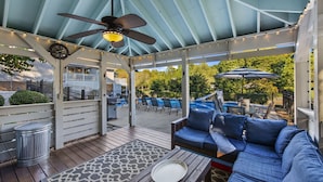 A covered patio area with a ceiling fan, string lights, a seating area with a sofa and chairs, and a view of a backyard with a pool and lounge chairs. - Lake Norman Luxury - Large Saltwater Pool, Dock & Boathouse - Sleeps 18 (Denver)