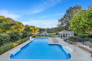 A swimming pool with a gazebo, lounge chairs, and a view of a park and buildings in the background.