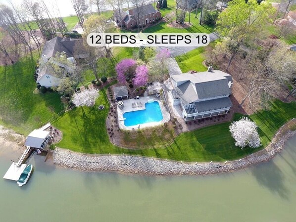 A large house with a swimming pool, surrounded by a well-maintained lawn and trees.