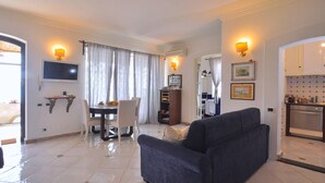 A living room with a sofa, a dining table with chairs, a TV mounted on the wall, and a kitchen area with cabinets and a stove. - Star Fish House - Two Bedroom Villa, Sleeps 5 (San Cosma)