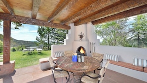 An outdoor patio with a round table and chairs, a fireplace, and a view of the surrounding landscape. - Ponderosa Estate | Secluded Luxury (Santa Fe)