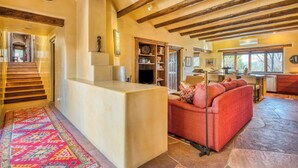 A spacious living area with a red sofa, a wooden staircase, and a kitchen in the background. - Ponderosa Estate | Secluded Luxury (Santa Fe)