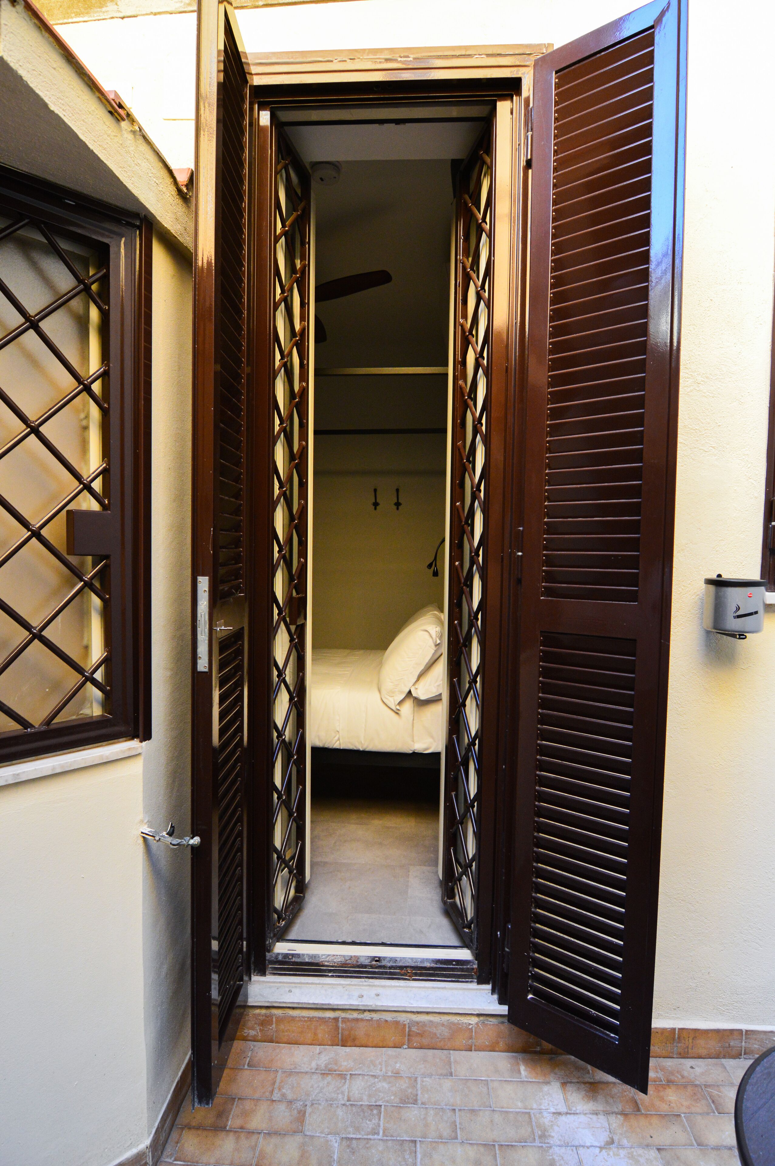 A narrow hallway with a bed at the end, flanked by two open doors with louvered shutters.