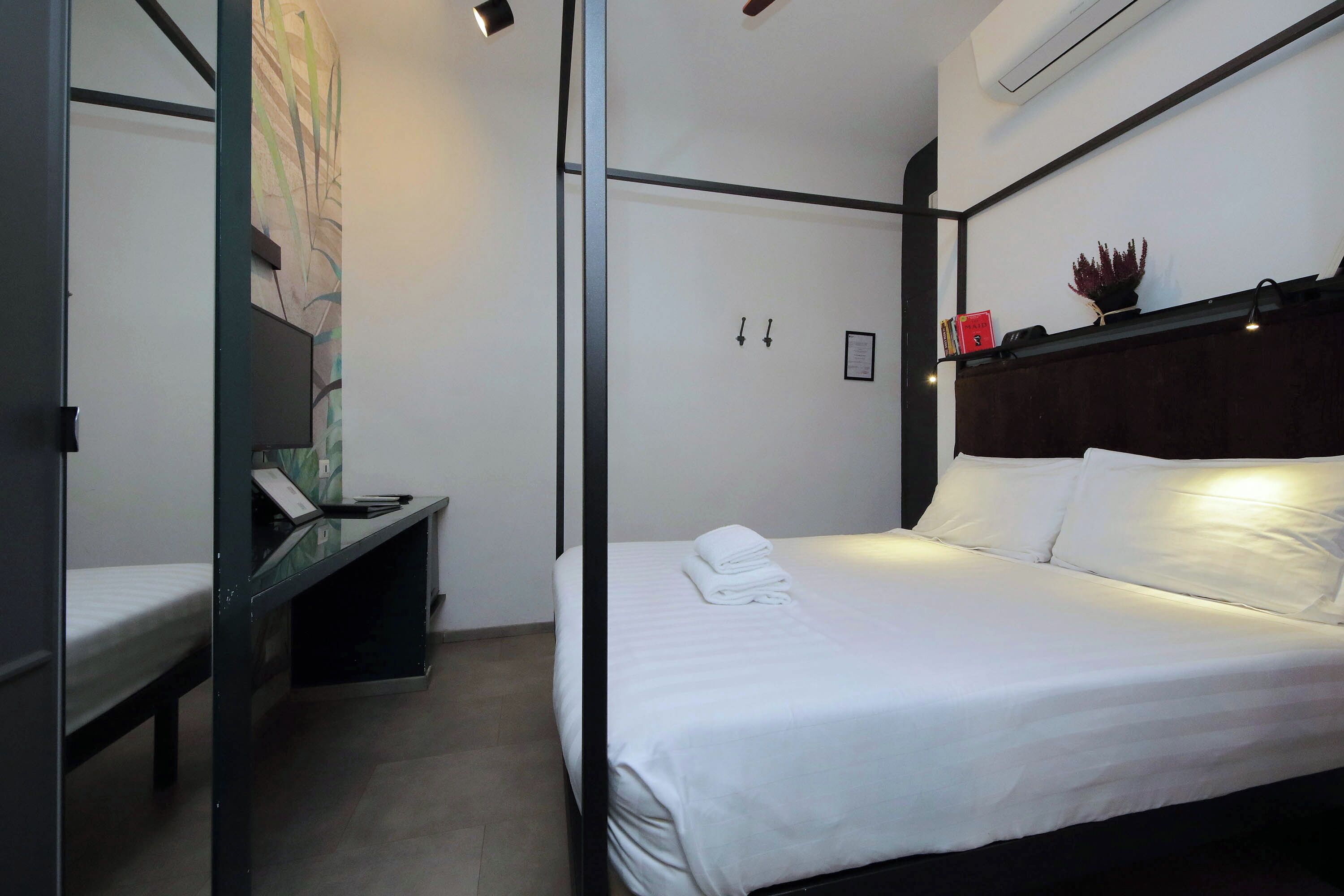 Een moderne hotelkamer met een opgemaakt bed, een bureau met stoel, en een tv aan de muur.