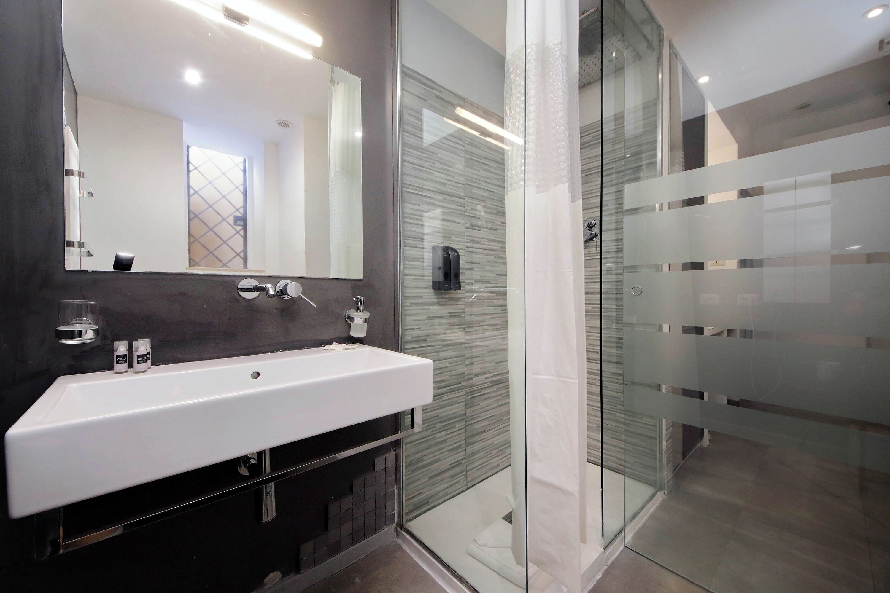 Une salle de bain moderne avec un lavabo blanc, un grand miroir et une cabine de douche en verre.