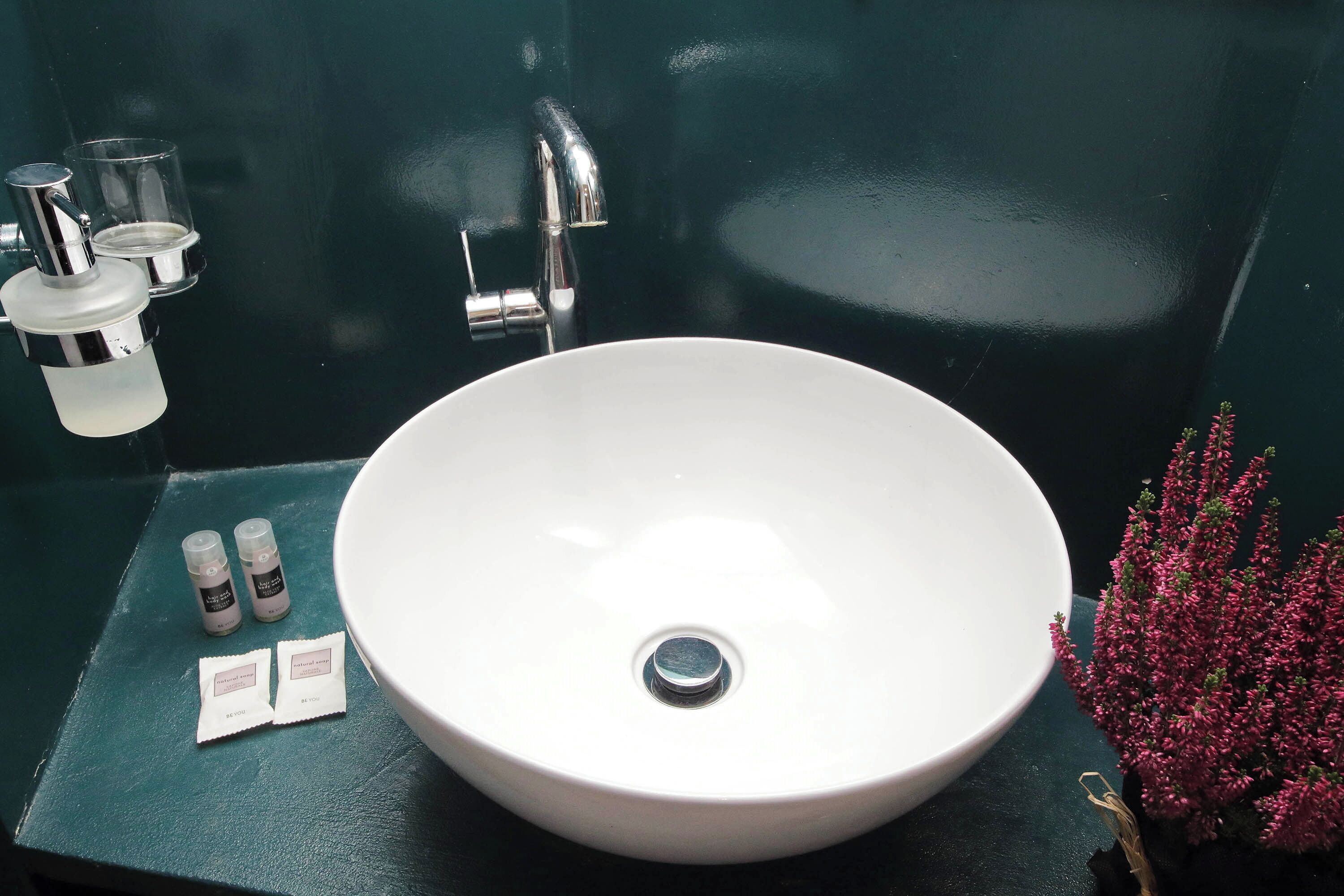 A white sink with a chrome faucet, two small bottles, and two packets on a green countertop.