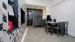 Een moderne keuken met een donker aanrecht, een koffieapparaat en een eethoek met een tafel en stoelen.