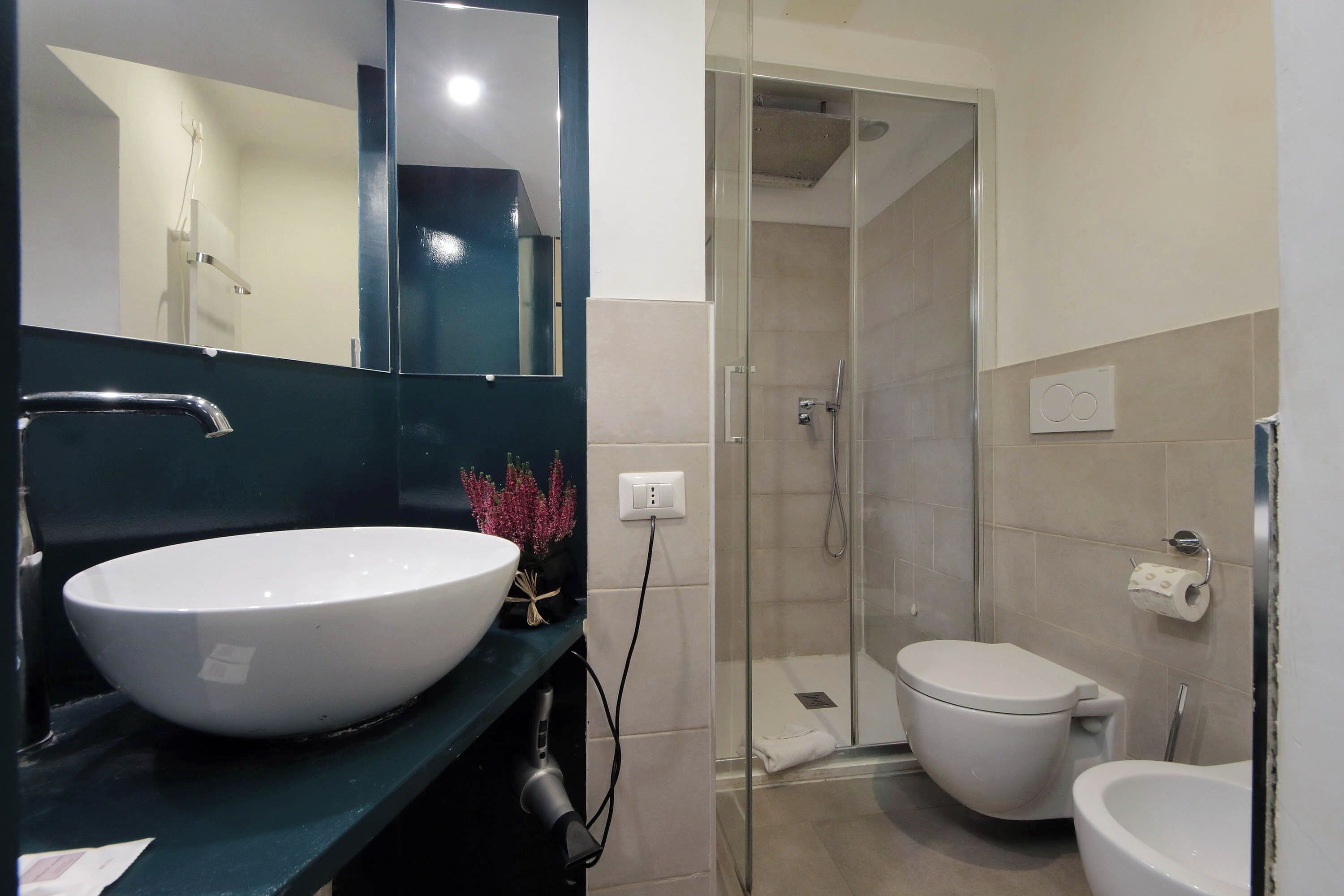 A modern bathroom with a large white sink, a glass-enclosed shower, and a white toilet.