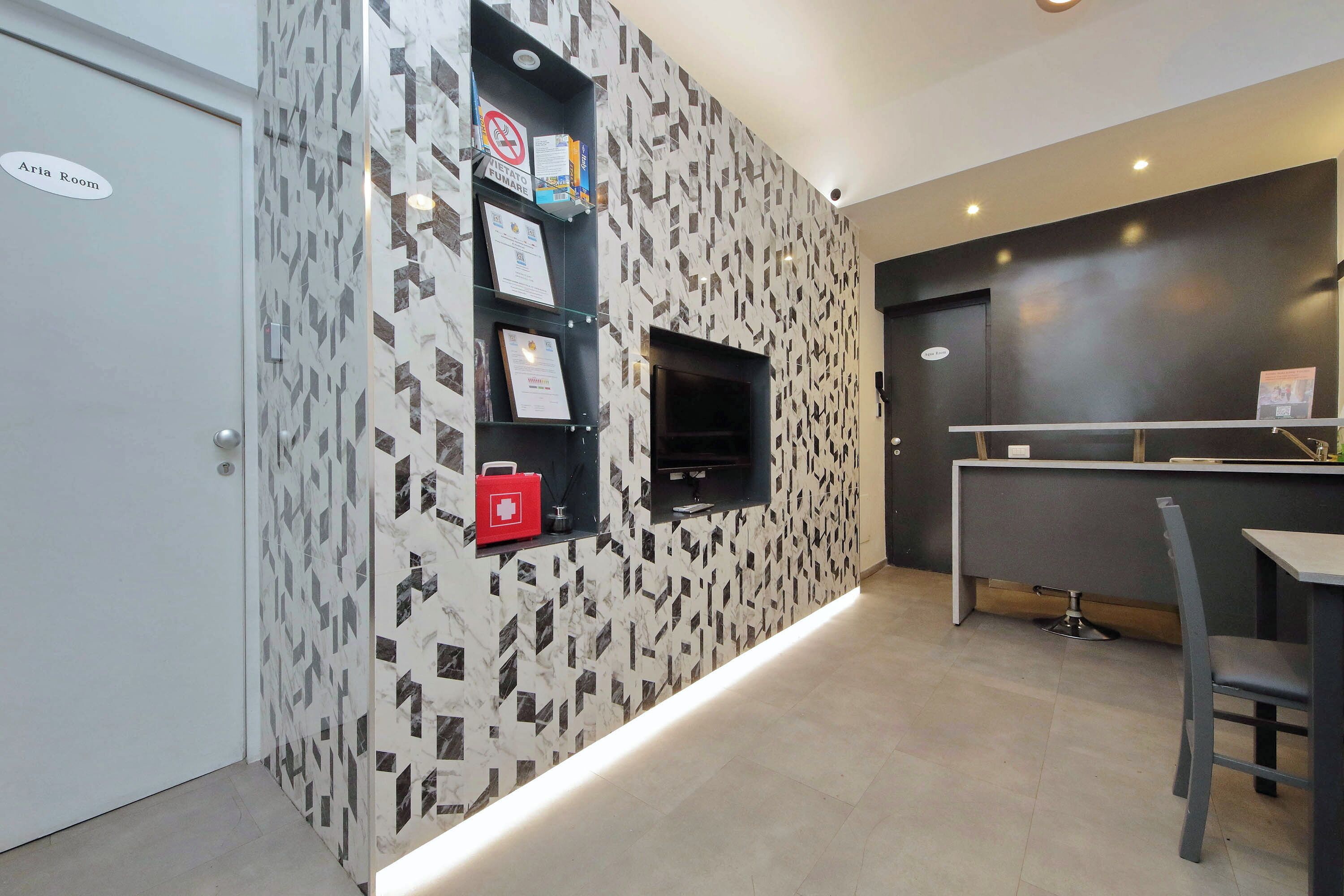 A modern hotel room with a geometric patterned wall, a small TV, and a reception desk with a chair.