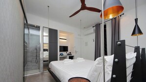 Een moderne hotelkamer met een bed, een rond tafel, een plafondventilator en een badkamer met een glazen deur.
