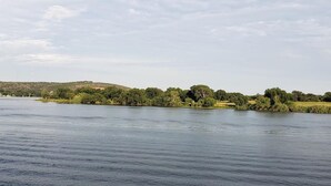 A calm river with a forested bank and distant hills.