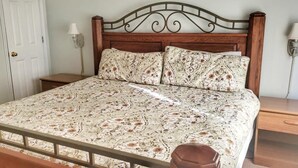 Un lit avec une couvre-lit à motifs, une tête de lit en bois, deux tables de chevet et des lampes fixées au mur.