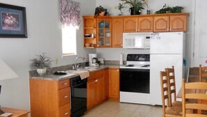 Une cuisine de taille réduite, dotée de meubles en bois, d’un four à micro-ondes, d’un réfrigérateur et d’un ventilateur de plafond.